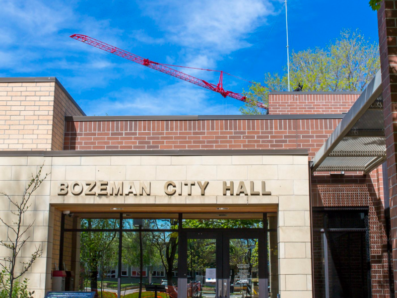 A photo of Bozeman City Hall with a large red crane rising above in the background.